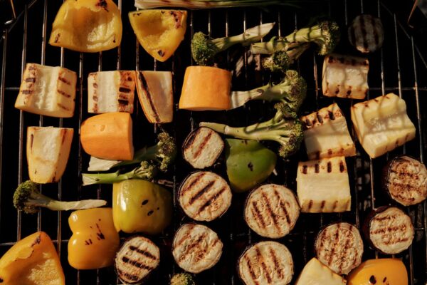 Assorted grilled vegetables including peppers, eggplant, and broccoli on a barbecue grill.