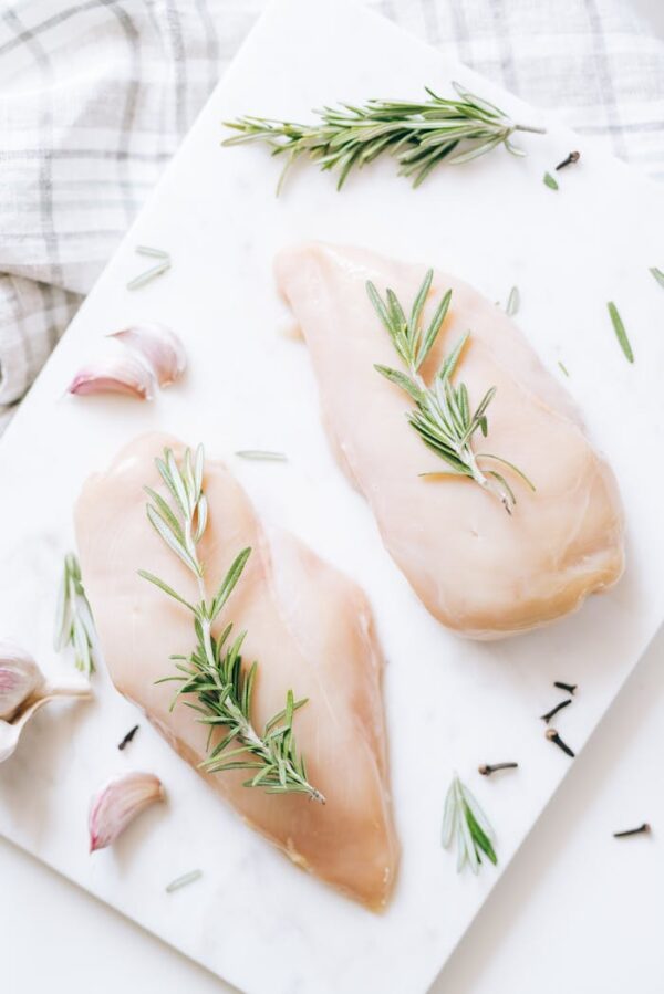 High-angle view of raw chicken breasts on marble with rosemary and garlic, ideal for healthy recipe inspiration.